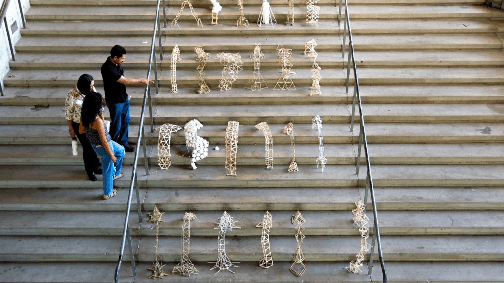 Students observing a stairway exhibit of small-scale architectural structures made from various materials