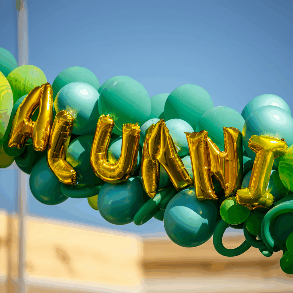 Gold balloon letters spelling 'ALUMNI' surrounded by green balloons at a Cal Poly alumni event.