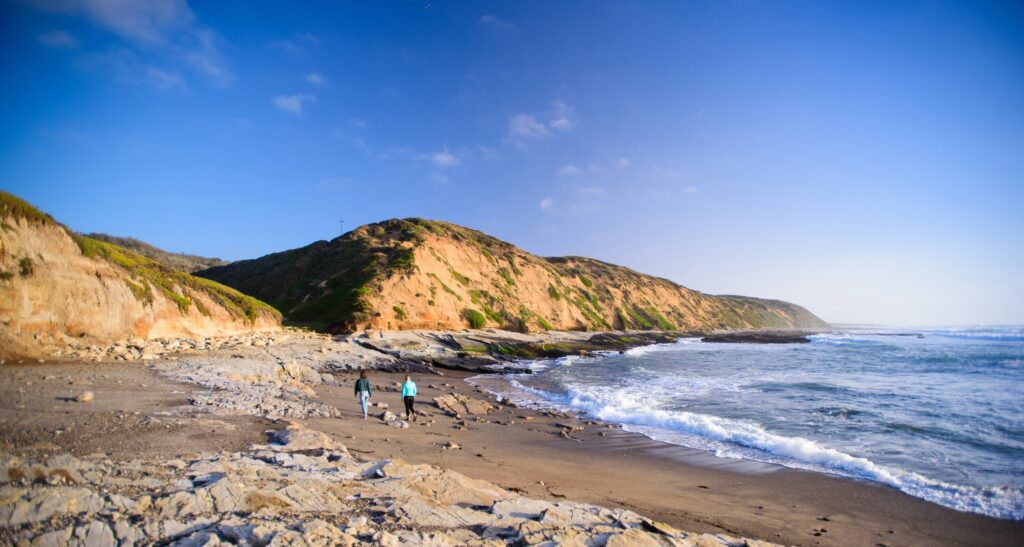 People walking along a rugged beach trail near coastal cliffs at sunset near San Luis Obispo