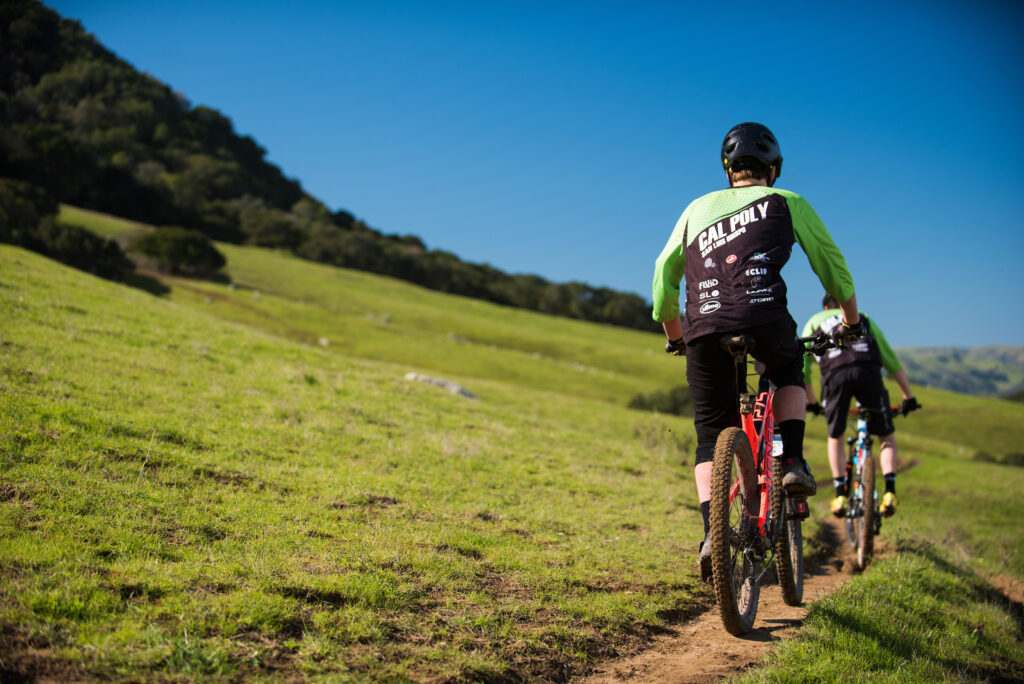 Students mountain biking on a grassy trail near Cal Poly with hills in the background