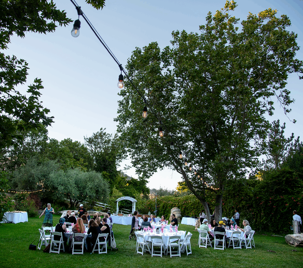 Guests seated at white tables for an outdoor garden dinner under string lights at Cal Poly