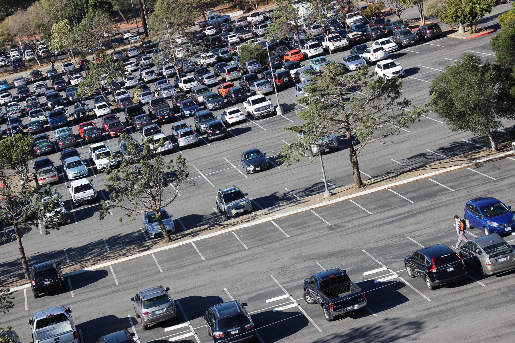 Overhead view of a busy Cal Poly parking lot filled with parked vehicles and surrounded by trees.