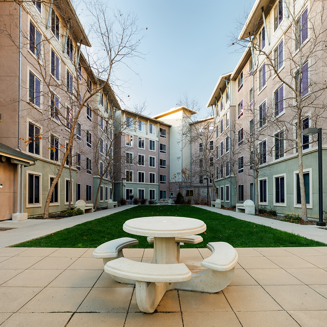 Courtyard at Cal Poly's Poly Canyon Village featuring modern student housing, green lawn, and round concrete picnic table