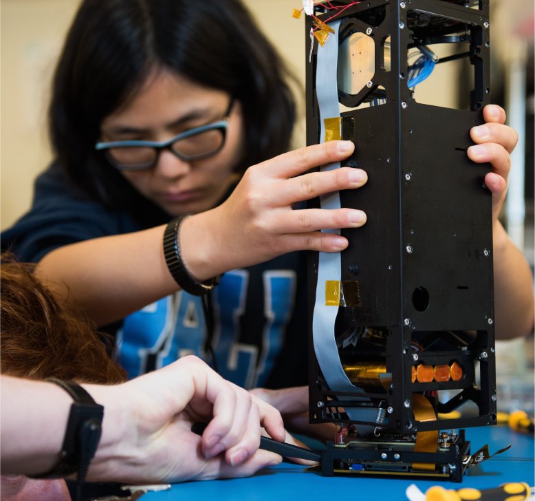 Student assembling a CubeSat satellite prototype during a Cal Poly engineering project