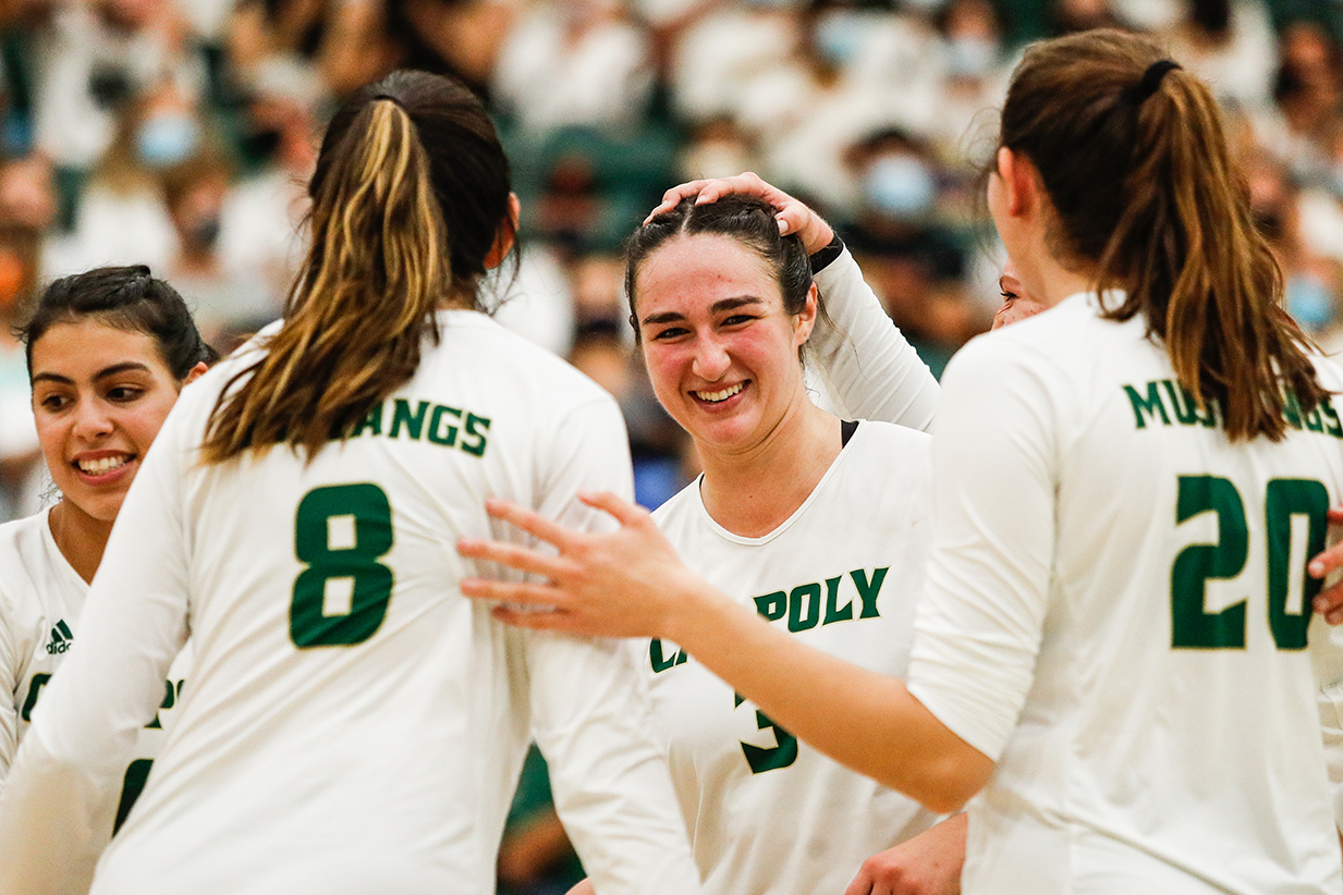 Cal Poly women's volleyball players in white jerseys celebrating during a game