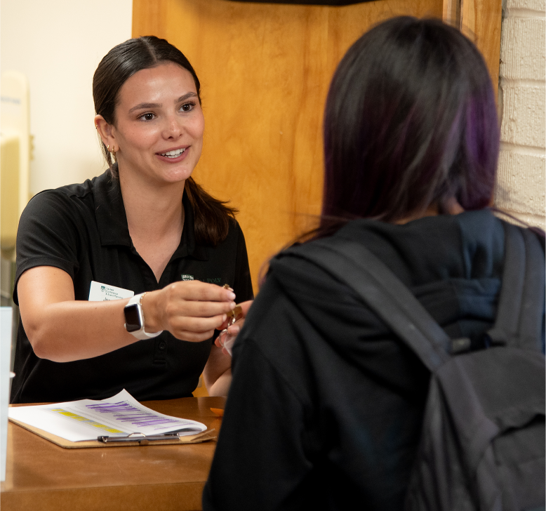 Staff member greeting a student at a campus check-in welcome desk