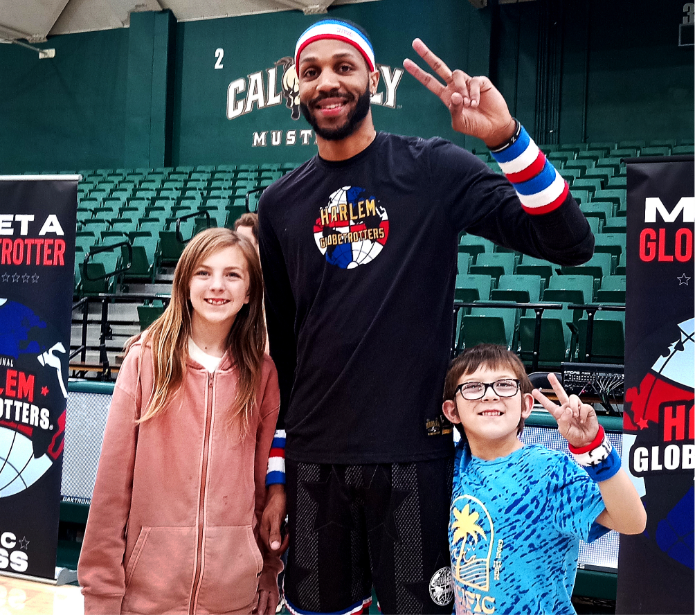Two kids posing with a Harlem Globetrotter player in a gymnasium