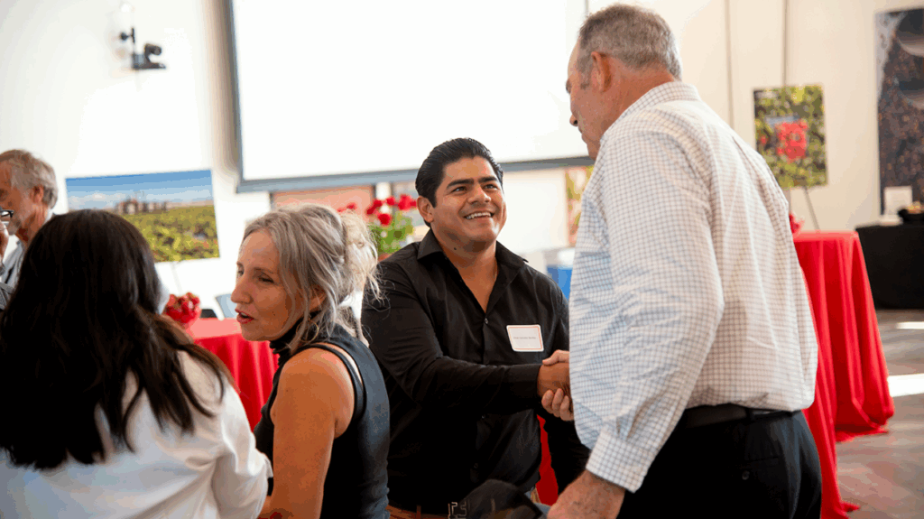 Attendees shaking hands and smiling during a Cal Poly wine and agriculture networking event